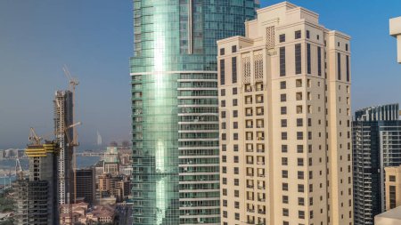 Téléchargez les photos : Gratte-ciel modernes dans la résidence Jumeirah plage à Dubaï, JBR timelapse aérien avec palmier Jumeirah sur un fond pendant le coucher du soleil. Soleil réfléchi par la surface du verre - en image libre de droit