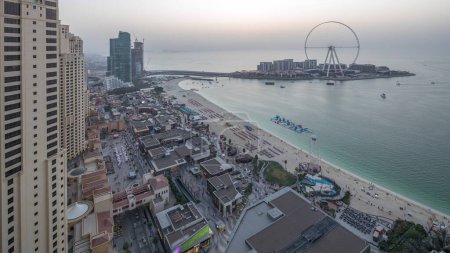Waterfront overview Jumeirah Beach Residence JBR skyline aerial day to night transition timelapse with illuminated skyscrapers. Shops, restaurants and other entertainment from above