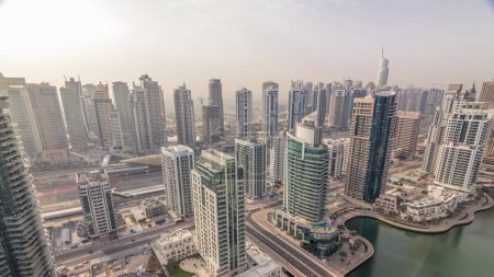 Aerial top view of Dubai Marina and JLT morning timelapse. Promenade and canal with floating yachts and boats after sunrise in Dubai, UAE. Modern towers and traffic on the road