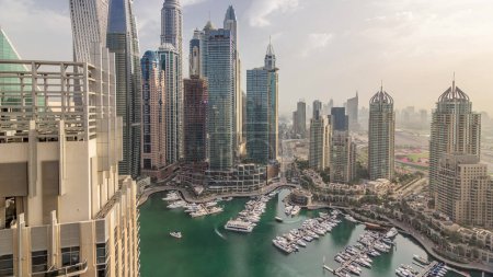Aerial top view of Dubai Marina morning timelapse. Promenade and canal with floating yachts and boats after sunrise in Dubai, UAE. Modern towers and traffic on the road