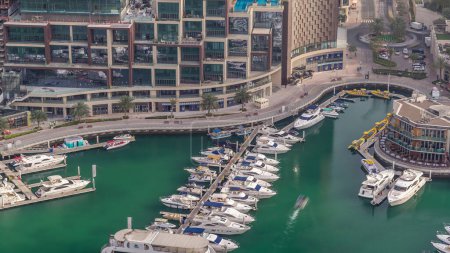 Luftaufnahme von Yachten, die im Zeitraffer in Dubais Marina schwimmen. Weiße Boote stehen im grünen Kanalwasser. Promenade mit Geschäften und Restaurants.
