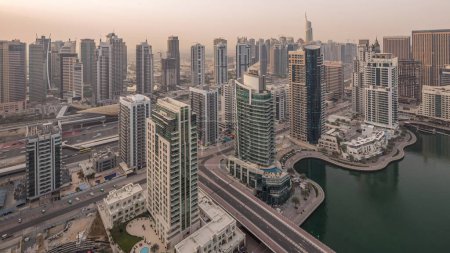 Aerial top view of Dubai Marina and JLT morning timelapse. Promenade and canal with floating yachts and boats after sunrise in Dubai, UAE. Modern towers and traffic on the road