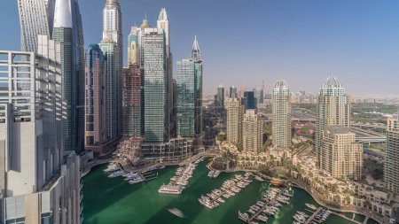 Aerial top view of Dubai Marina evening timelapse. Promenade and canal with floating yachts and boats before sunset in Dubai, UAE. Modern towers and traffic on the road