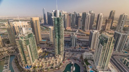 Aerial top view of Dubai Marina and JLT evening timelapse. Promenade and canal with floating yachts and boats before sunset in Dubai, UAE. Modern towers and traffic on the road