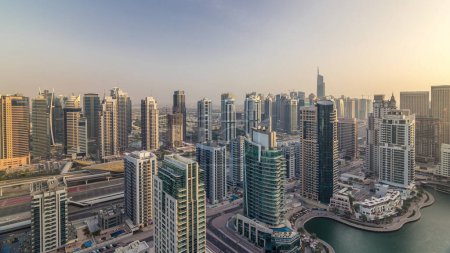 Aerial top view of Dubai Marina and JLT evening timelapse. Promenade and canal with floating yachts and boats before sunset in Dubai, UAE. Modern towers and traffic on the road