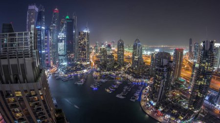 Foto de Vista aérea superior del timelapse de transición nocturna de Dubai Marina. Paseo marítimo y canal con yates flotantes y barcos en Dubai, Emiratos Árabes Unidos. Torres modernas iluminadas y el tráfico en la carretera - Imagen libre de derechos
