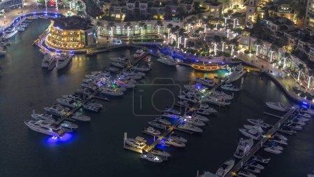 Luftaufnahme von Yachten, die im nächtlichen Zeitraffer in Dubais Marina schwimmen. Weiße Boote sind im Kanalwasser. beleuchtete Promenade mit Geschäften und Restaurants.