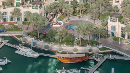 Luftaufnahme von Yachten, die im Zeitraffer in Dubais Marina schwimmen. Weiße Boote stehen im grünen Kanalwasser. Promenade mit Brunnen und Restaurants.