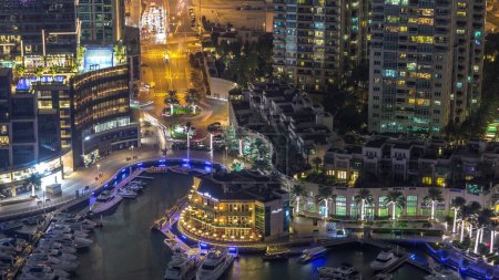 Téléchargez les photos : Vue aérienne sur les yachts flottant dans la marina de Dubaï timelapse de nuit. Trafic sur une route. Promenade éclairée avec commerces et restaurants
. - en image libre de droit