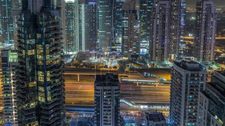 Vista aérea superior del puerto deportivo de Dubái y el timelapse nocturno de JLT. Rascacielos de arriba en Dubai, Emiratos Árabes Unidos. Torres modernas iluminadas y el tráfico en la carretera
