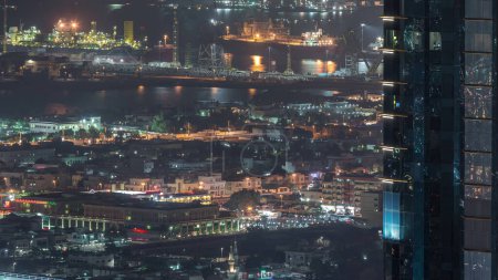 Photo for Aerial view from Downtown of Dubai night timelapse with skyscrapers, houses and port Rashid on a background, ships docking at sea port, UAE - Royalty Free Image