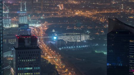Foto de Vista aérea al distrito financiero y zabeel noche a día con el tráfico y en construcción edificio con grúas del centro de Dubai. Deira en un segundo plano. Rascacielos iluminados antes del amanecer - Imagen libre de derechos