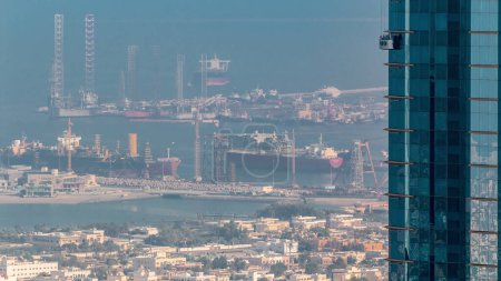 Foto de Vista aérea de la mañana desde el centro de Dubái timelapse con limpiadores de ventanas en rascacielos, casas y puerto Rashid en un segundo plano, barcos atracando en el puerto marítimo, Emiratos Árabes Unidos - Imagen libre de derechos