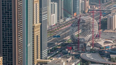 Lugar de construcción del Museo del Futuro con grúas aéreas matutinas timelapse, próximo edificio icónico de Dubai. Los rascacielos y el tráfico en la carretera en el fondo
