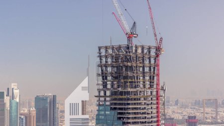 Téléchargez les photos : Progrès de construction du nouveau gratte-ciel moderne dans la ville de Dubaï timelapse aérien, Émirats arabes unis. Grues et matériel de construction dans le quartier financier près du centre-ville - en image libre de droit