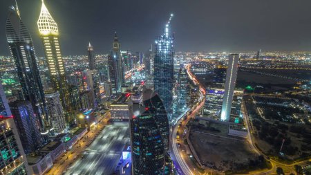 Panoramic skyline of the buildings near Sheikh Zayed Road and DIFC during night aerial in Dubai, UAE. Modern towers and illuminated skyscrapers with lights switching in financial center and downtown