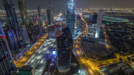 Foto de Skyline panorámico de los edificios cerca de Sheikh Zayed Road y DIFC timelapse noche aérea en Dubai, Emiratos Árabes Unidos. Modernas torres y rascacielos iluminados en el centro financiero y el centro - Imagen libre de derechos