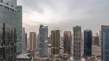 Foto de Edificios residenciales y de oficinas en Jumeirah lago torres distrito día a noche timelapse transición en Dubai. Vista panorámica aérea desde arriba con rascacielos modernos - Imagen libre de derechos
