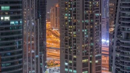 Edificios residenciales y de oficinas en Jumeirah lago torres distrito noche timelapse con luces parpadeantes en las ventanas de Dubai. Vista aérea desde arriba con rascacielos modernos
