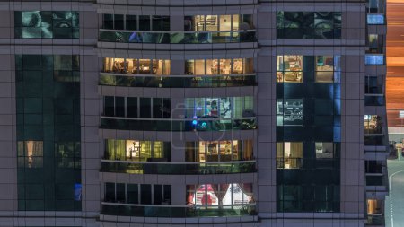 Vista nocturna del apartamento exterior timelapse edificio. Rascacielos de gran altura con luces parpadeantes en ventanas con personas moviéndose dentro
