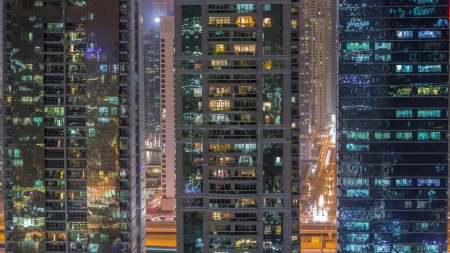 Téléchargez les photos : Des immeubles résidentiels et de bureaux dans le quartier Jumeirah Lake Towers Night Timelapse avec des lumières clignotantes dans les fenêtres à Dubaï. Vue aérienne d'en haut avec des gratte-ciel modernes - en image libre de droit