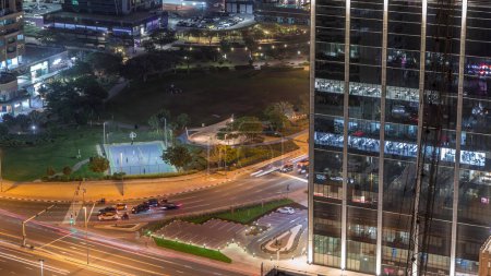 Téléchargez les photos : Bâtiments résidentiels et bureaux à Jumeirah Lake Towers quartier timelapse de nuit avec parc et la circulation à l'intersection à Dubaï. Vue panoramique aérienne d'en haut avec des gratte-ciel modernes - en image libre de droit