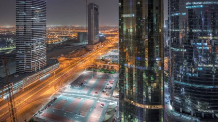 Photo for Office buildings in Jumeirah lake towers district night timelapse in Dubai. Aerial panoramic view from above with modern skyscrapers, traffic on a road and parking - Royalty Free Image