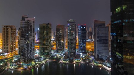 Foto de Edificios residenciales y de oficinas en el lago Jumeirah torres distrito noche a día timelapse transición antes del amanecer en Dubai. Vista panorámica aérea desde arriba con rascacielos modernos iluminados - Imagen libre de derechos