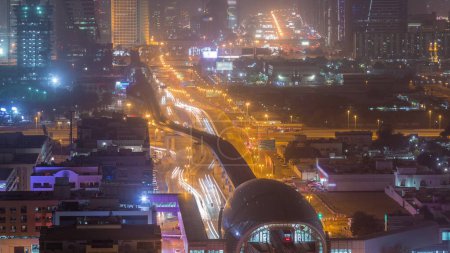Téléchargez les photos : Station de métro et la circulation sur la route de nuit timelapse. Vue aérienne depuis le haut du bâtiment. Sheikh Zayed Road à Dubaï et passerelle, gratte-ciel sur fond - en image libre de droit
