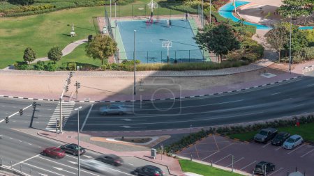 Photo for Basketball court at park in Jumeirah Lakes Towers aerial timelapse, a popular residential district towards the southern end of Dubai. Green lawn and traffic on intersection from above. - Royalty Free Image