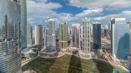 Foto de Apartamentos y oficinas residenciales en Jumeirah lago torres distrito timelapse en Dubai. Vista panorámica aérea desde arriba con rascacielos modernos y nubes en el cielo azul - Imagen libre de derechos