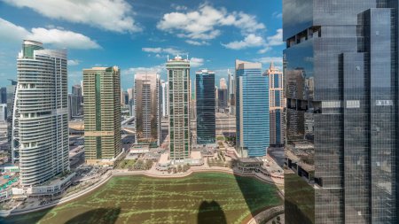 Photo for Residential apartments and offices in Jumeirah lake towers district timelapse in Dubai. Aerial panoramic view from above with modern skyscrapers and clouds on blue sky - Royalty Free Image
