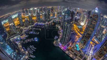 Dubai Marina illuminated skyscrapers and jumeirah lake towers panoramic view from the top aerial night timelapse in the United Arab Emirates. Traffic on a road and floating boats