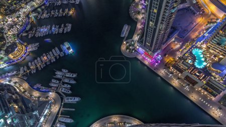 Photo for Dubai Marina harbor with modern yachts near waterfront aerial night timelapse from top. Floating boats on canal surrounded towers and skyscrapers. - Royalty Free Image