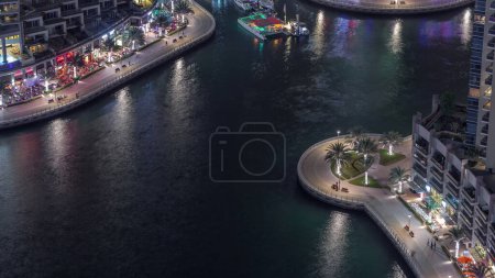 Téléchargez les photos : Promenade au bord de l'eau avec palmiers et restaurants à Dubai Marina timelapse de nuit aérienne. Bateaux et yachts flottant sur le canal. Dubai, Émirats arabes unis - en image libre de droit