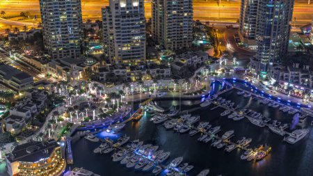 Photo for Dubai Marina harbor with modern yachts near waterfront aerial night timelapse. Floating boats on canal surrounded towers and skyscrapers. - Royalty Free Image