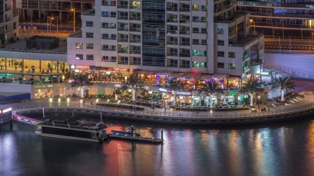 Téléchargez les photos : Promenade au bord de l'eau avec restaurants à Dubai Marina timelapse de nuit aérienne. Bateaux et yachts flottant sur le canal. Dubai, Émirats arabes unis - en image libre de droit