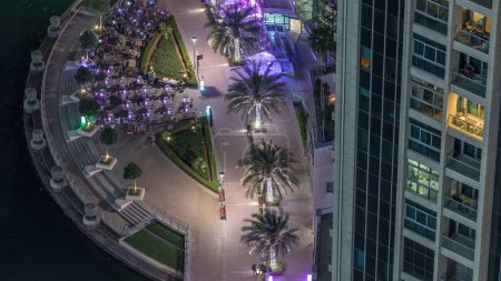 Téléchargez les photos : Promenade au bord de l'eau avec cafés à Dubai Marina timelapse de nuit aérienne. Bateaux et yachts flottant sur le canal. Dubai, Émirats arabes unis - en image libre de droit