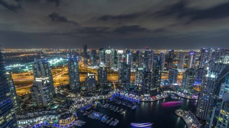 Foto de Dubai Marina iluminó rascacielos y torres de lago jumeirah vista panorámica desde la parte superior aérea toda la noche con luces apagadas en los Emiratos Árabes Unidos. Tráfico por carretera y yates flotantes - Imagen libre de derechos