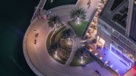 Téléchargez les photos : Cercle de promenade au bord de l'eau avec palmiers à Dubai Marina timelapse de nuit aérienne. Bateaux et yachts flottant sur le canal. Dubai, Émirats arabes unis - en image libre de droit