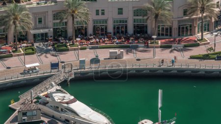 Photo for Waterfront promenade with restaurants in Dubai Marina aerial timelapse. Boats and yachts floating on canal. Dubai, United Arab Emirates - Royalty Free Image