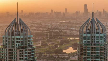 Sunrise over Dubai Marina skyscrapers and golf course view from the top aerial morning timelapse in the United Arab Emirates. Orange haze
