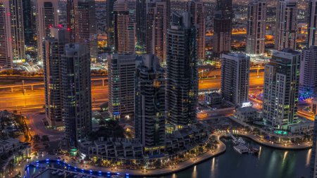Dubai Marina illuminated skyscrapers and jumeirah lake towers view from the top aerial night to day transition timelapse in the United Arab Emirates. Traffic on a road