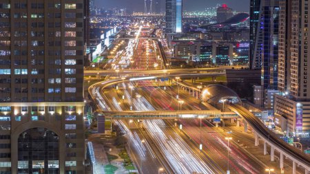 Téléchargez les photos : Skyline ville internet avec croisement Sheikh Zayed Road timelapse de nuit aérienne. gratte-ciel éclairés avec circulation sur une autoroute et une ligne de métro à Dubaï - en image libre de droit