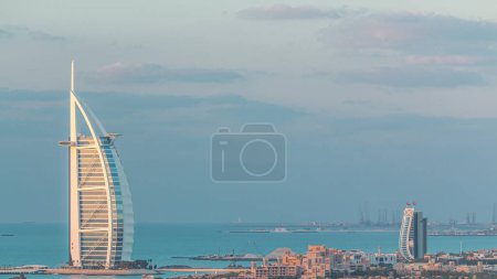 Téléchargez les photos : Vue aérienne de l'hôtel Burj Al Arab de la ville de l'Internet jour à la nuit transition timelapse. Yachts et bateaux sur fond. Ciel nuageux - en image libre de droit