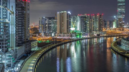 Téléchargez les photos : Vue aérienne des tours dans la ville lumineuse la nuit timelapse avec beau canal et front de mer à Business Bay, Dubai, Émirats arabes unis - en image libre de droit