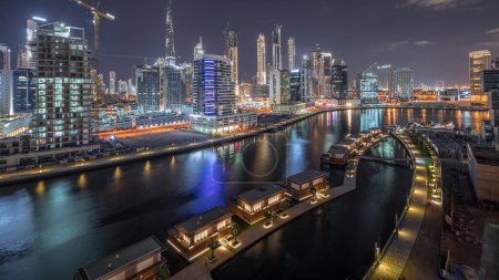 Téléchargez les photos : Vue panoramique aérienne du canal dans la ville la nuit brillante près de bâtiments de luxe canal dans Business Bay timelapse avec gratte-ciel du centre-ville, Dubaï, Émirats arabes unis - en image libre de droit