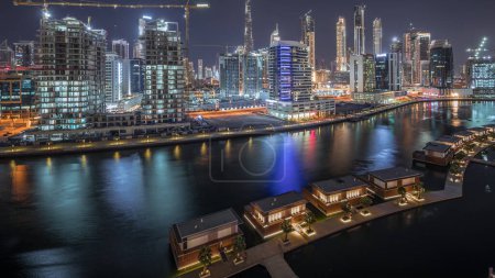 Téléchargez les photos : Vue d'horizon de la grande ville avec des routes et des rues lumineuses et des gratte-ciel élevés de Business Bay et du centre-ville la nuit près du canal timelapse aérien, Dubaï, Émirats arabes unis - en image libre de droit