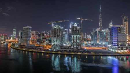 Photo for Skyline of the city at night with beautiful canal with reflections and bright skyscrapers aerial timelapse in Business Bay, Dubai, United Arab Emirates. Towers under construction - Royalty Free Image