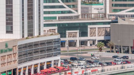 Foto de Aparcamiento y restaurante cerca del canal en Dubai timelapse aéreo en un día soleado con palmeras en la costa con rascacielos en un fondo en Business Bay, Dubai, Emiratos Árabes Unidos - Imagen libre de derechos
